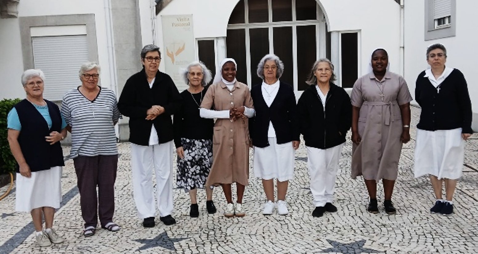 As nove irmãs da comunidade de Braga, de pé, lado a lado, num pátio de calçada portuguesa.